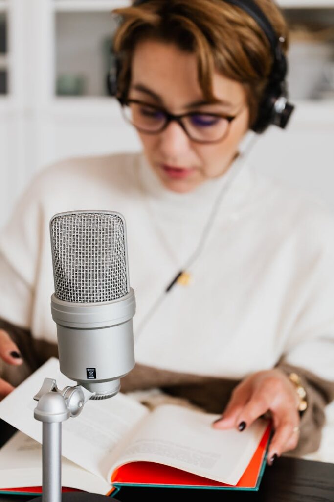 Focused woman reading aloud into microphone, recording audiobook in cozy setting.